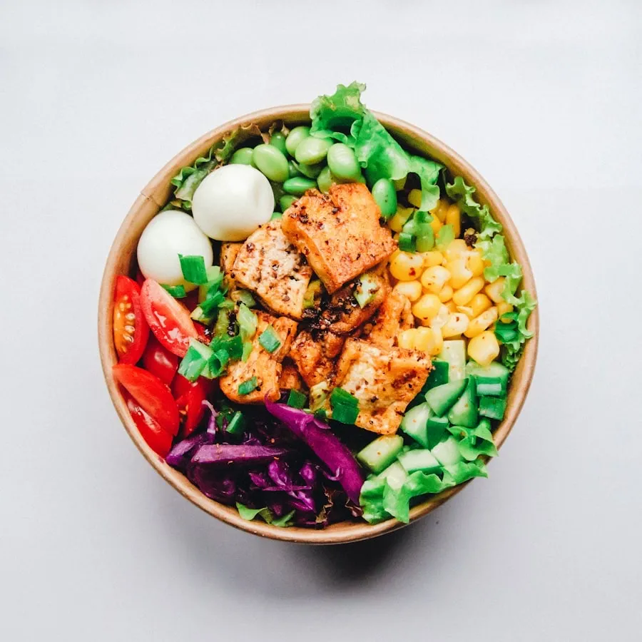 Bowl of grilled chicken, boiled eggs, edamame, sweet corn, cherry tomatoes, red cabbage and leafy greens
